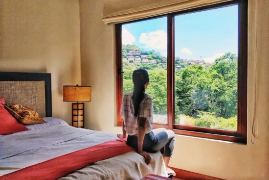 Woman looking out to the green forest from window in a Playa Hermosa Costa Rica Airbnb