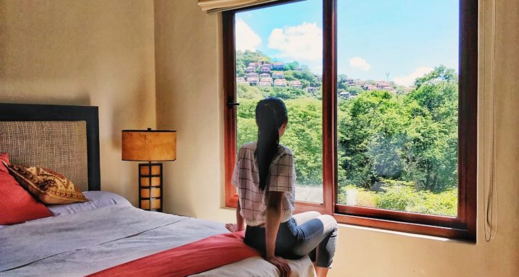 Woman looking out to the green forest from window in a Playa Hermosa Costa Rica Airbnb