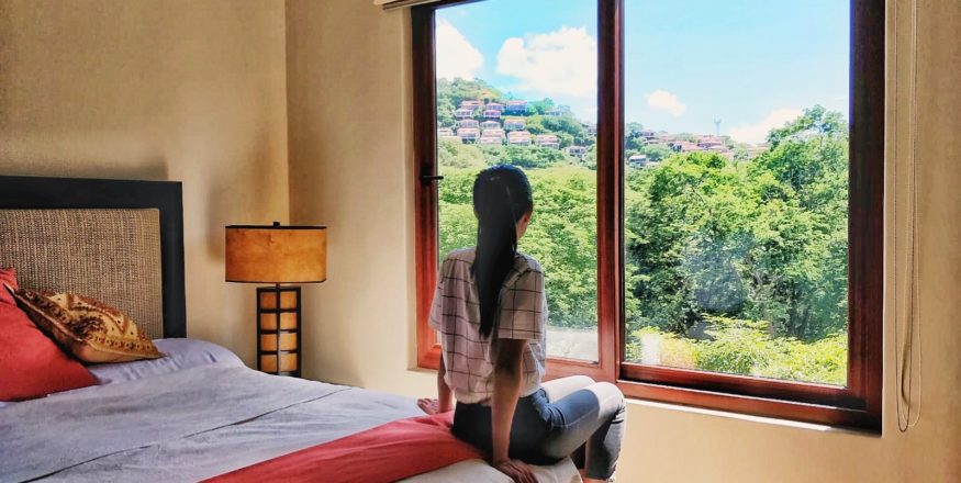 Woman looking out to the green forest from window in a Playa Hermosa Costa Rica Airbnb